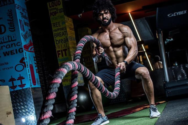 An image of a bodybuilder man doing battling ropes